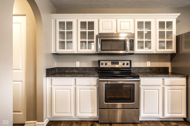 6114 Pebblebrooke Rd, Whitestown, IN 46075 - kitchen featuring appliances with stainless steel finishes, white cabinets, arched walkways, glass insert cabinets, and dark stone countertops