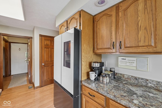 6983 White Oak Dr, Avon, IN 46123 - kitchen with refrigerator, light wood-style floors, brown cabinetry, dark stone countertops, and a textured ceiling
