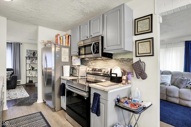 2832 Hillside Ave, Indianapolis, IN 46218 - kitchen with appliances with stainless steel finishes, backsplash, gray cabinets, light wood-style flooring, and a textured ceiling
