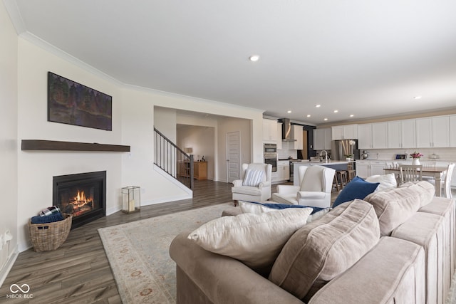 living area with wood finished floors, baseboards, a glass covered fireplace, crown molding, and recessed lighting
