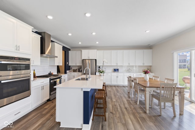 kitchen with appliances with stainless steel finishes, wall chimney range hood, a sink, tasteful backsplash, and ornamental molding