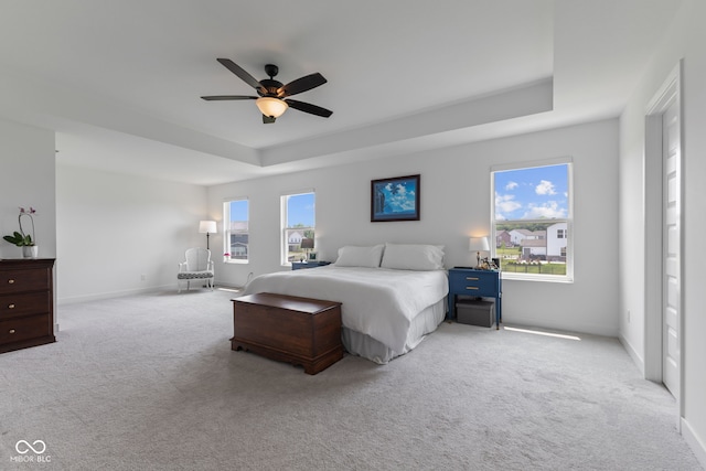carpeted bedroom featuring a tray ceiling, baseboards, and ceiling fan