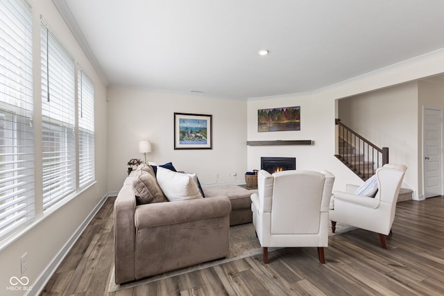 living area featuring a warm lit fireplace, wood finished floors, crown molding, baseboards, and stairway