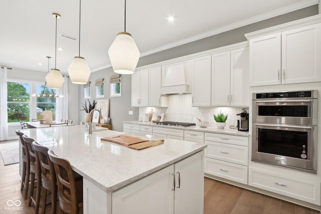 12594 Pasco St, Fishers, IN 46038 - kitchen with appliances with stainless steel finishes, custom range hood, an island with sink, white cabinetry, and healthy amount of natural light