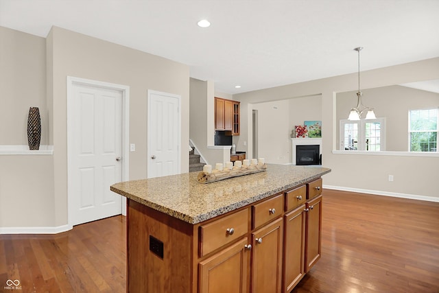 13528 Cuppertino Ln, Carmel, IN 46074 - kitchen with dark wood-style flooring, brown cabinets, a glass covered fireplace, a center island, and pendant lighting