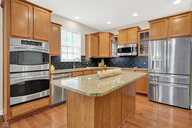 13528 Cuppertino Ln, Carmel, IN 46074 - kitchen featuring appliances with stainless steel finishes, light wood finished floors, a kitchen island, decorative backsplash, and recessed lighting