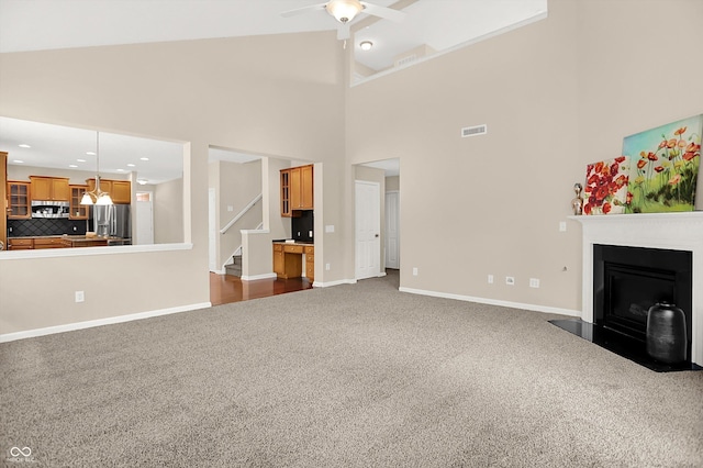 13528 Cuppertino Ln, Carmel, IN 46074 - unfurnished living room featuring dark colored carpet, a fireplace with flush hearth, stairway, high vaulted ceiling, and a ceiling fan