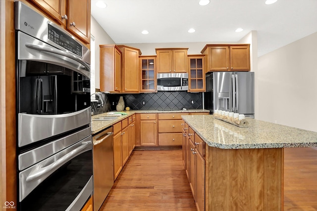 13528 Cuppertino Ln, Carmel, IN 46074 - kitchen featuring appliances with stainless steel finishes, a center island, light wood finished floors, light stone countertops, and tasteful backsplash