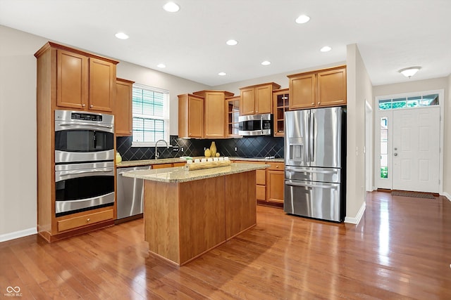 13528 Cuppertino Ln, Carmel, IN 46074 - kitchen featuring appliances with stainless steel finishes, light wood-style floors, backsplash, a kitchen island, and glass insert cabinets