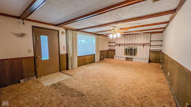 3215 E 10th St, Anderson, IN 46012 - unfurnished living room featuring wainscoting, beam ceiling, ceiling fan, a fireplace, and wooden walls
