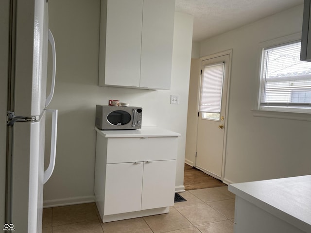 1444 N Denny St, Indianapolis, IN 46201 - kitchen featuring stainless steel microwave, freestanding refrigerator, light countertops, white cabinetry, and light tile patterned floors