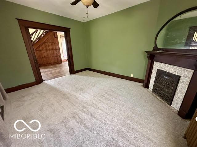 323 W 8th St, Rushville, IN 46173 - unfurnished living room featuring carpet flooring, baseboards, ceiling fan, and a fireplace