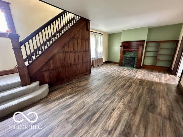 323 W 8th St, Rushville, IN 46173 - unfurnished living room with radiator heating unit, stairway, wood finished floors, baseboards, and a fireplace