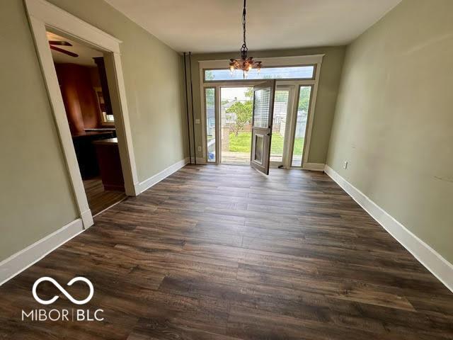 323 W 8th St, Rushville, IN 46173 - unfurnished dining area featuring dark wood-style flooring, a chandelier, and baseboards
