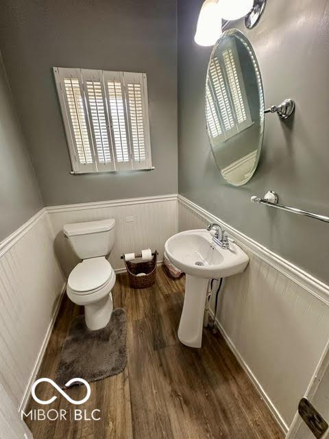 323 W 8th St, Rushville, IN 46173 - half bathroom with a wainscoted wall, wood finished floors, toilet, and plenty of natural light