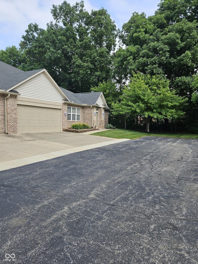 6956 Park Square Dr Unit D, Avon, IN 46123 - view of front facade with brick siding, an attached garage, driveway, a shingled roof, and view of scattered trees