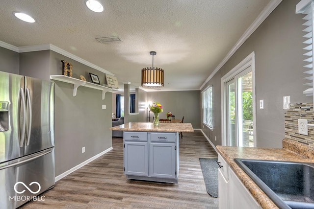 7657 Wheatgrass Ln, Noblesville, IN 46062 - kitchen with stainless steel refrigerator with ice dispenser, wood finished floors, ornamental molding, healthy amount of natural light, and light countertops
