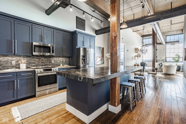 630 N College Ave Unit 409, Indianapolis, IN 46204 - kitchen featuring appliances with stainless steel finishes, rail lighting, a towering ceiling, tasteful backsplash, and a kitchen bar