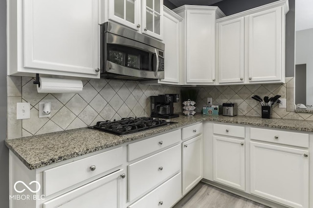 2502 Colinbrook Pkwy, Greenwood, IN 46143 - kitchen with stainless steel microwave, white cabinets, tasteful backsplash, black gas cooktop, and light stone countertops