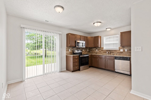 1903 Windy Hill Ln, Indianapolis, IN 46239 - kitchen featuring appliances with stainless steel finishes, backsplash, a textured ceiling, light stone countertops, and light tile patterned flooring