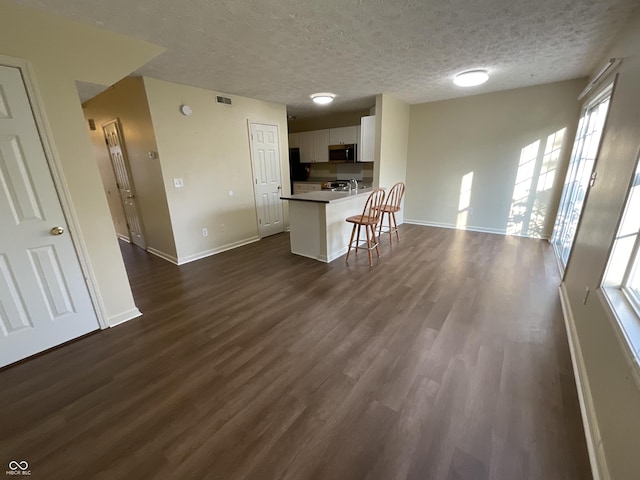 2853 S Walnut Street Pike, Bloomington, IN 47401 - kitchen with stainless steel microwave, white cabinetry, dark wood-type flooring, a breakfast bar, and a textured ceiling