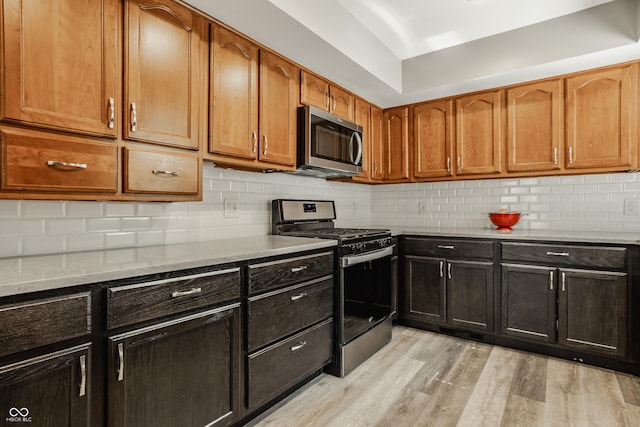 4428 Edinburgh Pt, Indianapolis, IN 46228 - kitchen featuring appliances with stainless steel finishes, light wood-style flooring, backsplash, light stone countertops, and brown cabinets