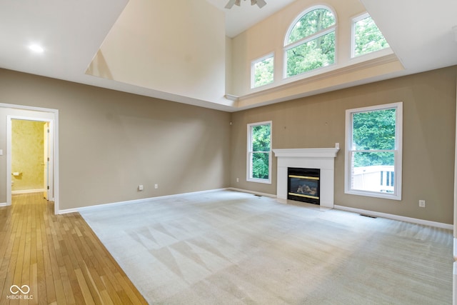 11036 Ravenna Way, Indianapolis, IN 46236 - unfurnished living room with a towering ceiling, baseboards, a glass covered fireplace, healthy amount of natural light, and light wood-style flooring