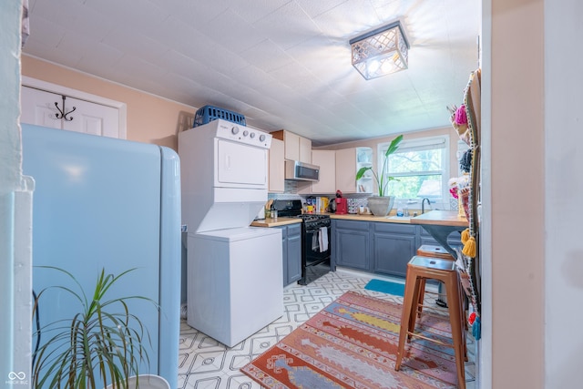 1101 S Rogers St, Bloomington, IN 47403 - kitchen featuring estacked washer and dryer, black range oven, stainless steel microwave, light countertops, and freestanding refrigerator