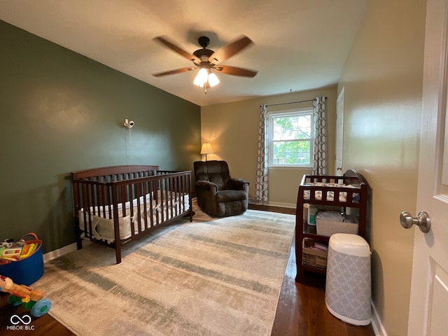 3520 Lantern Ln, Columbus, IN 47203 - bedroom with baseboards, a crib, wood finished floors, and a ceiling fan