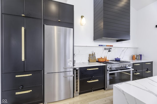 8695 Morgan Dr, Fishers, IN 46038 - kitchen featuring appliances with stainless steel finishes, wall chimney exhaust hood, light wood-style floors, light stone counters, and dark cabinetry