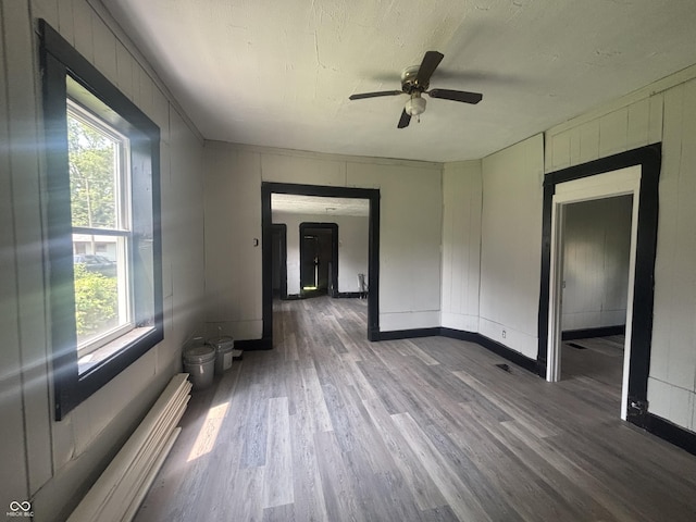 2826 Station St, Indianapolis, IN 46218 - unfurnished room with wood finished floors, ceiling fan, baseboard heating, baseboards, and a decorative wall