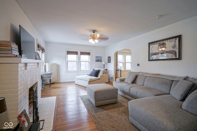 5435 E 10th St, Indianapolis, IN 46219 - living room featuring arched walkways, wood finished floors, a ceiling fan, a fireplace, and baseboards