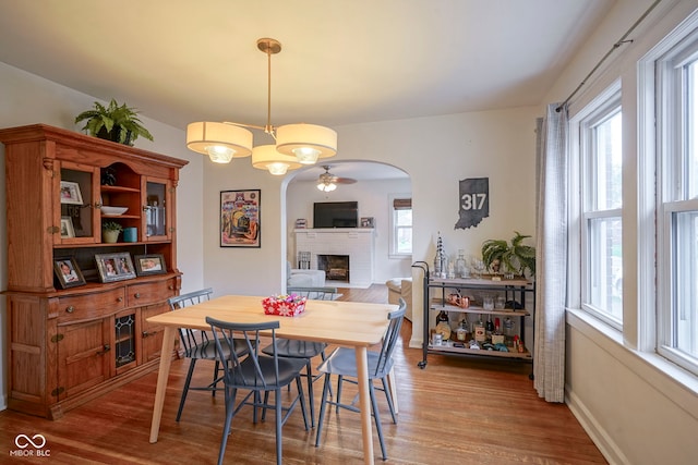 5435 E 10th St, Indianapolis, IN 46219 - dining area with arched walkways, wood finished floors, a fireplace, a ceiling fan, and baseboards