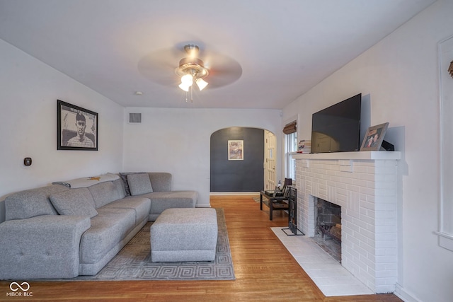 5435 E 10th St, Indianapolis, IN 46219 - living room featuring arched walkways, a fireplace, a ceiling fan, light wood-style floors, and baseboards