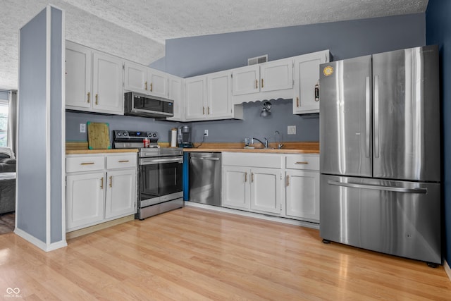 5811 Simmul Cir, Indianapolis, IN 46221 - kitchen with stainless steel appliances, a textured ceiling, light wood-type flooring, white cabinetry, and light countertops