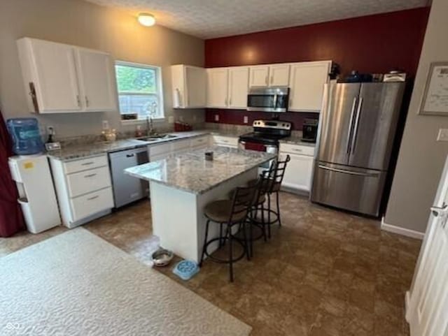 1711 Jaques Dr, Lebanon, IN 46052 - kitchen with appliances with stainless steel finishes, a textured ceiling, a sink, white cabinetry, and a kitchen bar