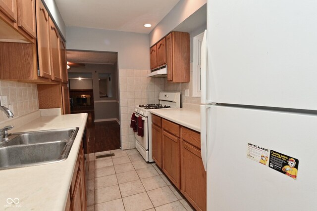 4751 N Longworth Ave, Indianapolis, IN 46226 - kitchen featuring white appliances, under cabinet range hood, a sink, brown cabinets, and light tile patterned flooring