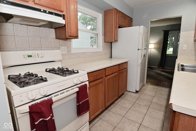 4751 N Longworth Ave, Indianapolis, IN 46226 - kitchen with white appliances, under cabinet range hood, light tile patterned floors, and brown cabinets