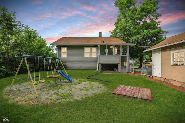 1915 Albany St, Beech Grove, IN 46107 - back of house at dusk with a playground, a sunroom, a lawn, and a chimney