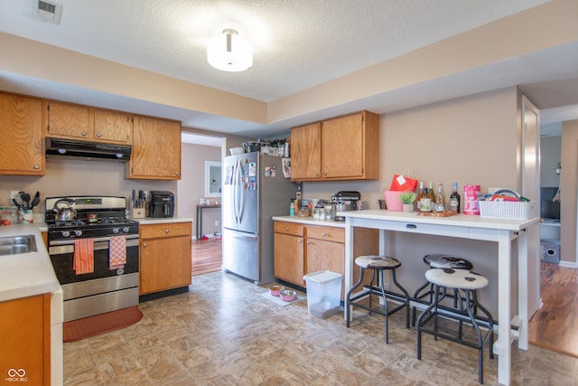8056 Maple Stream Blvd, Indianapolis, IN 46217 - kitchen featuring stainless steel appliances, under cabinet range hood, light countertops, brown cabinets, and a textured ceiling