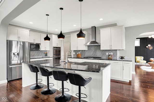 2789 W High Grove Cir, Zionsville, IN 46077 - kitchen with appliances with stainless steel finishes, wall chimney range hood, arched walkways, dark wood-style floors, and a center island with sink