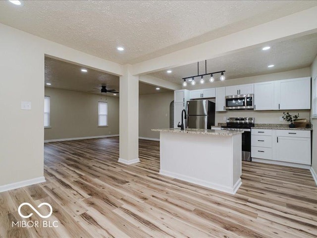 3558 N Gladstone Ave, Indianapolis, IN 46218 - kitchen with appliances with stainless steel finishes, light wood-type flooring, a textured ceiling, baseboards, and open floor plan