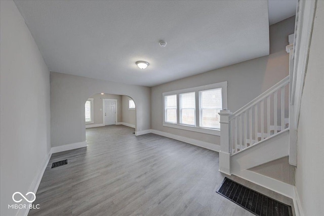 418 Eastern Ave, Indianapolis, IN 46201 - unfurnished living room with arched walkways, wood finished floors, and stairs