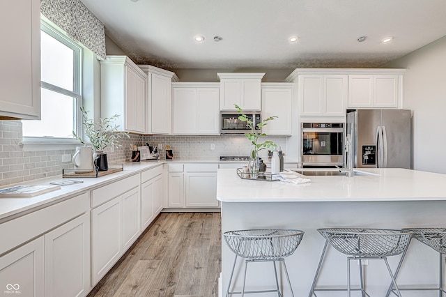 587 Bluestem Ln, New Whiteland, IN 46184 - kitchen with appliances with stainless steel finishes, white cabinets, a kitchen breakfast bar, backsplash, and light wood finished floors