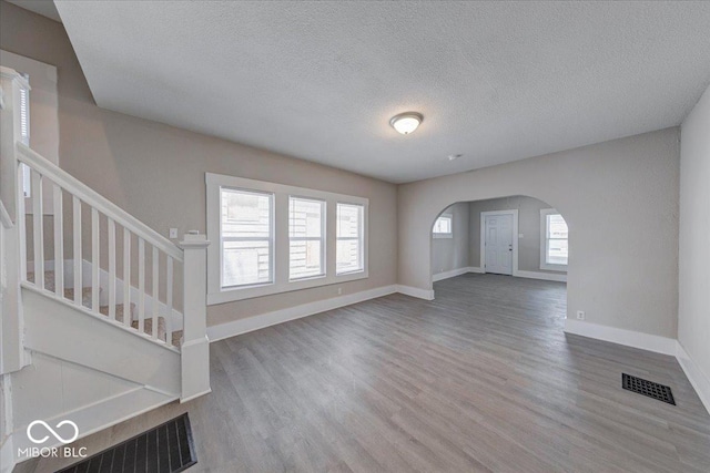 420 Eastern Ave, Indianapolis, IN 46201 - unfurnished living room featuring wood finished floors, arched walkways, stairs, and a textured ceiling