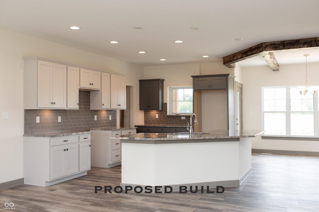 LOT30 Doe Mdw, Anderson, IN 46011 - kitchen featuring a sink, an island with sink, light stone counters, light wood-style floors, and decorative backsplash