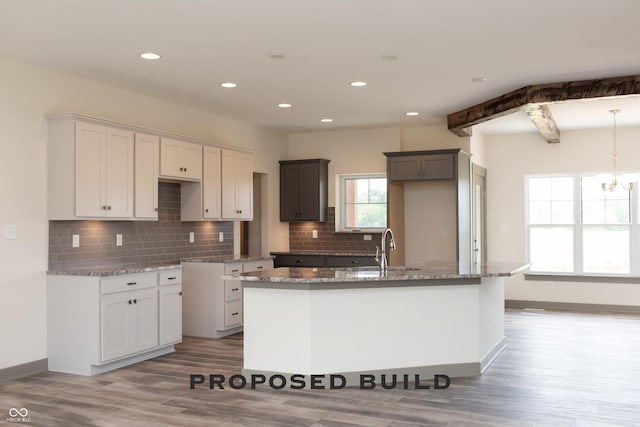 LOT30 Doe Mdw, Anderson, IN 46011 - kitchen featuring a sink, an island with sink, light stone counters, light wood-style floors, and decorative backsplash