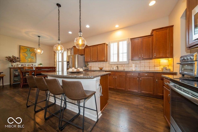 12976 Walbeck Dr, Fishers, IN 46037 - kitchen featuring appliances with stainless steel finishes, a breakfast bar area, a kitchen island, brown cabinetry, and recessed lighting