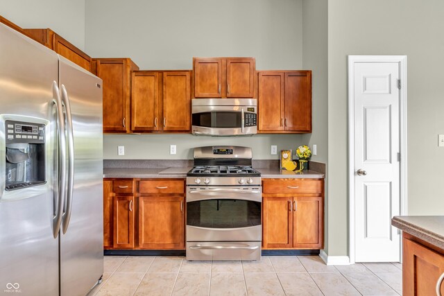 2948 Chalbury Dr, Plainfield, IN 46168 - kitchen featuring stainless steel appliances, light tile patterned flooring, brown cabinetry, dark countertops, and a towering ceiling