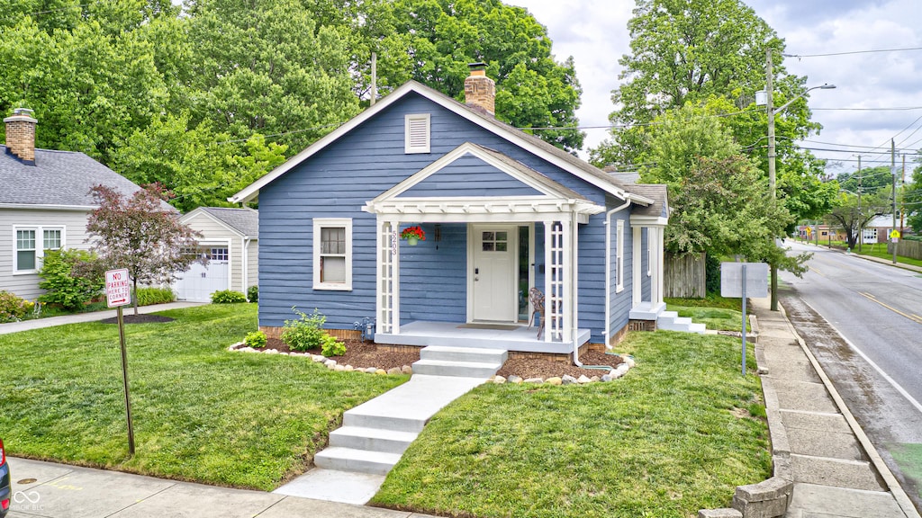 5203 Carrollton Ave, Indianapolis, IN 46220 - bungalow featuring covered porch, a chimney, a front lawn, and an outdoor structure